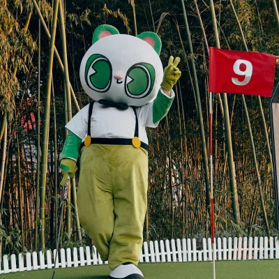 Beispiel für ein Maskottchenkostüm zum Herumlaufen: Figur mit übergroßem Kopf, Hemd, Hosenträgern und Hose auf einem Golfgrün